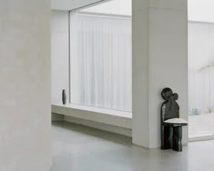 Modern minimalist interior design featuring concrete walls and floor, large frosted glass window, and a unique black chair wi