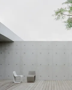 A minimalist outdoor space featuring a white and beige concrete wall and a wooden deck.