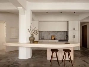 A minimalist residential kitchen with concrete island, stone walls, and modern appliances.