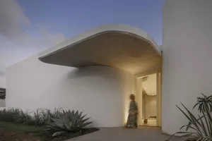 A modern residential entryway with a curved concrete canopy and ambient lighting.