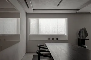 A minimalist interior design with a wooden dining table and chairs, featuring a large window with sheer curtains and a wall-m