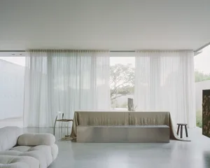 A modern living room with large windows, glass curtains, and concrete furniture.