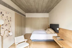 Modern minimalist bedroom with a white texture on the floor, walls, and furniture, featuring a bed with white bedding and a w