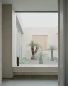 A minimalist living space with a large window showcasing a serene courtyard with palm trees.