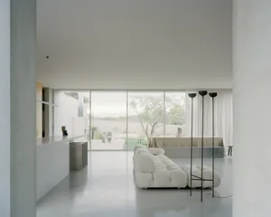 Modern minimalist living room with a white sofa, floor-to-ceiling windows, and a concrete floor.
