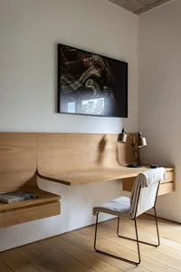 A minimalist workspace featuring a wooden desk and chair under a large framed abstract artwork.