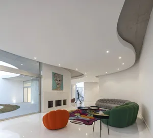 A modern living room with white concrete walls, colorful sofas and an abstract carpet.
