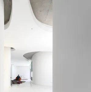 A modern, white, curved architectural space with a person sitting on an orange chair.