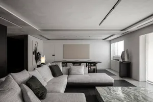A modern living room with concrete walls and floor, featuring a gray sectional sofa and a black marble coffee table.