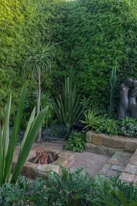 A landscaped garden with concrete paths, stone walls, gravel patio, and metal furniture.