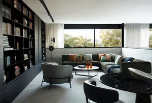 Modern minimalist living room with exposed concrete walls, a sectional couch, and a large bookshelf.
