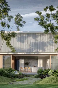 A minimalist residential exterior with metallic siding, framed by lush greenery and surrounded by clear blue sky.