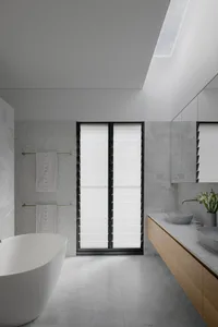 A modern bathroom with concrete tiles and marble features a large window, a freestanding tub, and a wooden vanity.