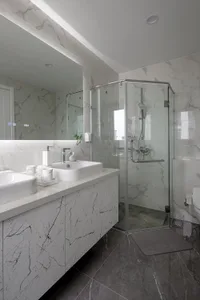 A modern bathroom with marble walls and floor, featuring a glass-enclosed shower, a floating vanity with white ceramic sinks,