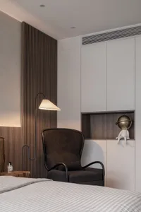 Modern bedroom with a dark wooden accent wall, a dark armchair, a floor lamp, and a white bed with striped sheets.
