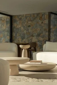 A modern living room featuring a textured concrete floor, white sofas, and a stone accent wall with natural stone tiles.