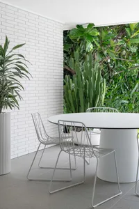 Modern dining room with metallic floor tiles, white brick wall, and large green plants.