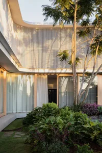 A modern house with a wooden panel exterior and a garden with lush green plants and a tree.