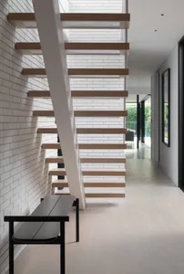 Modern floating staircase made of wood with a white brick wall and white flooring.