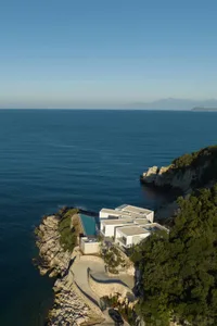 A modern house with concrete and glass façade overlooking the sea.
