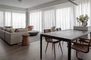 Modern industrial living room with wooden furniture and leather accents, featuring a large sofa, chairs, and a dining table.