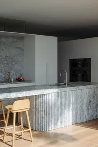Modern kitchen interior with marble island and stools.