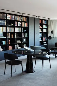 A modern library featuring marble bookshelves and a round black marble table with black leather chairs.