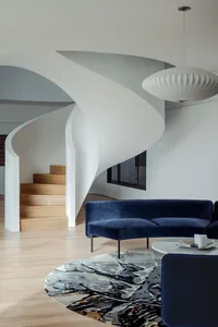 A modern living room featuring a navy blue velvet couch, a round coffee table, and a spiral staircase.