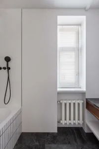 A modern minimalist bathroom with concrete elements, a window with blinds, and a radiator below it.