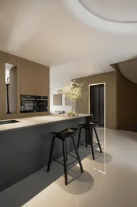 A minimalistic kitchen with concrete flooring and wooden cabinets, featuring a bar area with black stools and a vase of flowe