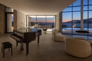 A modern minimalist living room featuring glass walls and large windows overlooking a scenic view.
