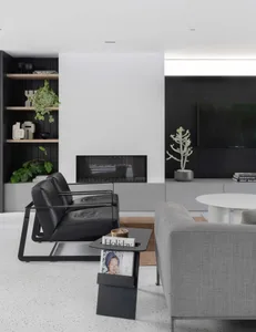 Minimalist living room furnished with black metal armchair and gray fabric sofa, featuring a modern fireplace, black shelving