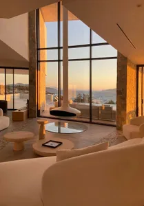 A modern residential home featuring a glass wall overlooking the sea at sunset.