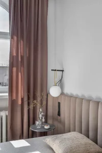 A modern bedroom featuring a beige upholstered headboard, gray curtains, and minimalist decor.