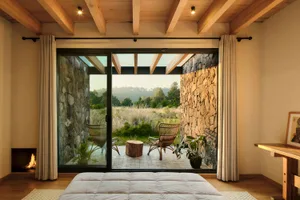 Modern bedroom featuring a stone patio view with wooden ceiling beams and a white bed.