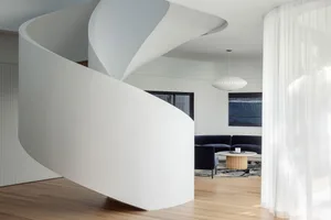 A modern, white, curved staircase made of concrete and wood materials.