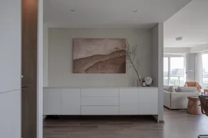 A modern living room with white furniture and a plant in a vase on a sideboard.