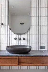 Modern minimalist bathroom with a black concrete sink, wooden vanity, and ceramic tiles with vertical lines.