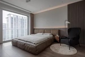 A minimalist bedroom featuring a large bed made of leather, a black armchair, and a round rug.