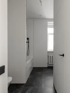 Modern minimalist white bathroom with black marble flooring and white tiled shower area.