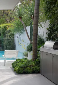 A modern patio featuring tropical greenery and a stainless steel grill.