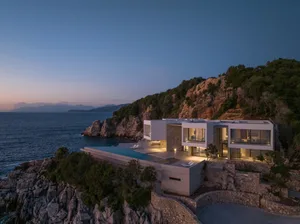 Modern minimalist vacation home with concrete exterior and infinity pool on a cliff side by the ocean.
