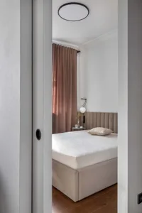A minimalist bedroom with a beige upholstered bed, brown velvet curtains, and wooden floor.