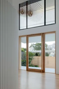 A minimalist living space featuring light-colored wood and glass doors, with a view of a green garden.