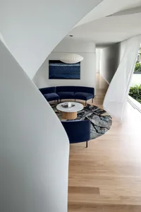 A modern living room with a dark blue fabric sectional sofa, a marble coffee table, and a round rug with a nature-inspired pa