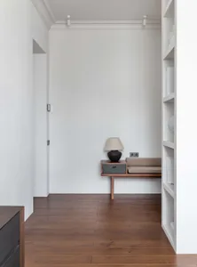 Modern minimalist living room with concrete and wood elements, featuring a cushioned nook with a table lamp and a shelf of ob