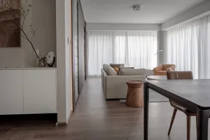 A modern living room with neutral-toned furniture and decor, featuring a large sofa, armchairs, and a dining table with chair