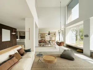 A minimalist living room with a white sofa, light wood coffee tables, and a concrete floor.