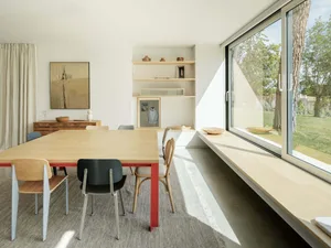 A modern dining room featuring sustainable wooden materials with a red-framed table and colorful chairs.