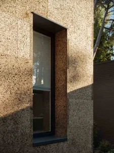 A modern minimalist house exterior featuring a textured concrete facade, tall vertical window, and shadow cast by sunlight.